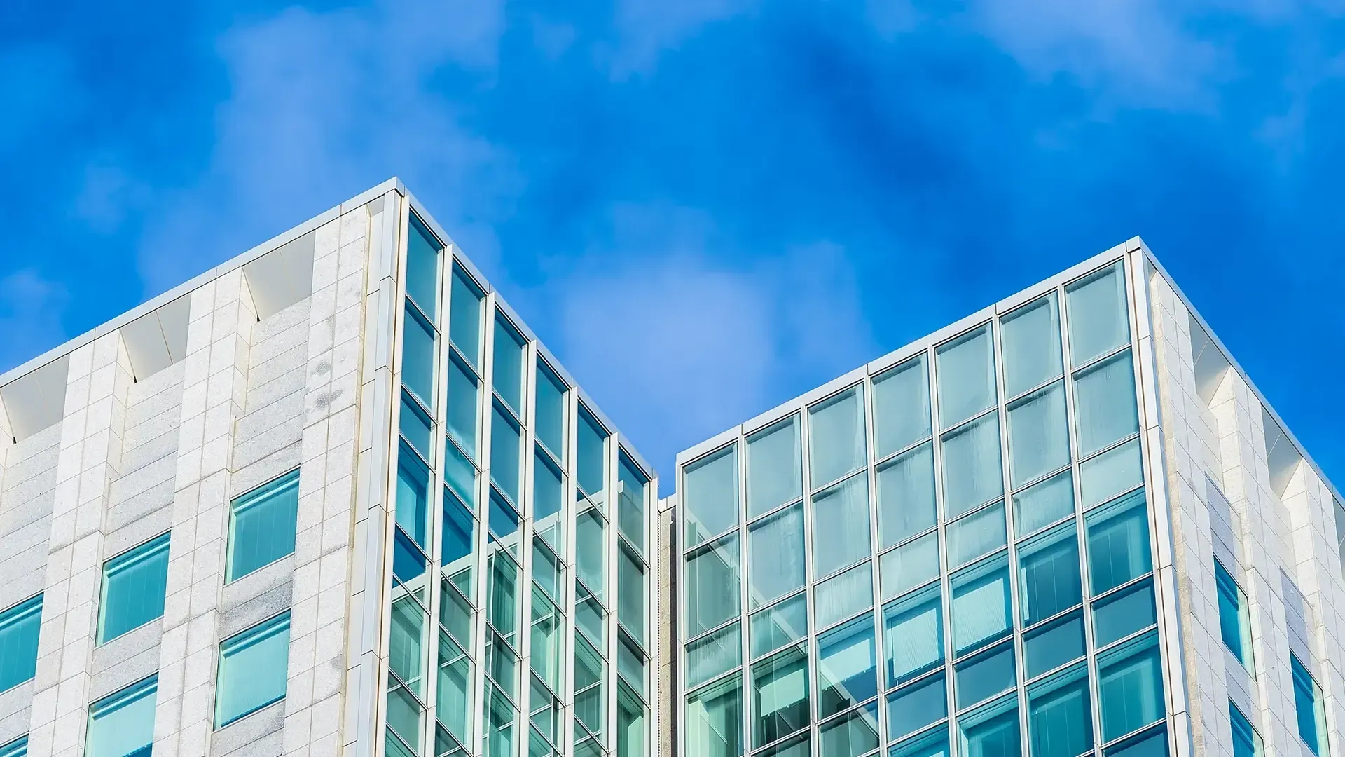 Two modern white buildings with glass windows against a bright blue sky.