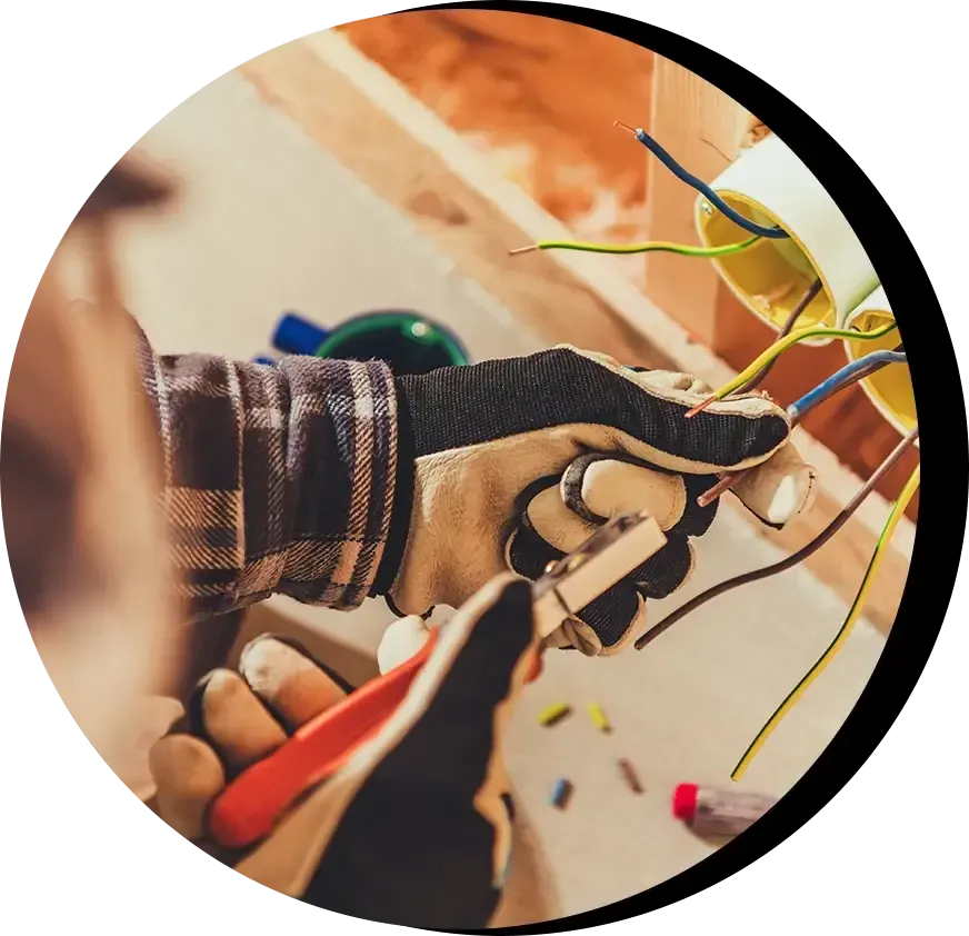 Electrician in gloves stripping wires in a wall-mounted junction box.