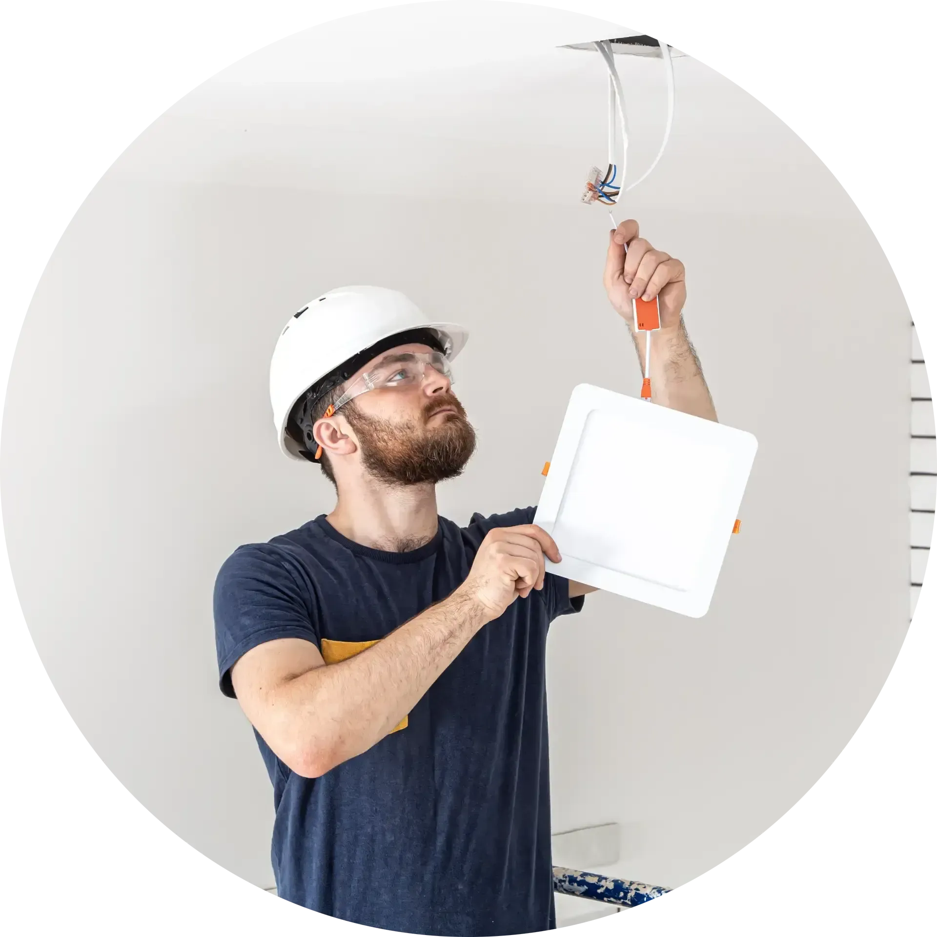 Electrician in hard hat installing ceiling light fixture.