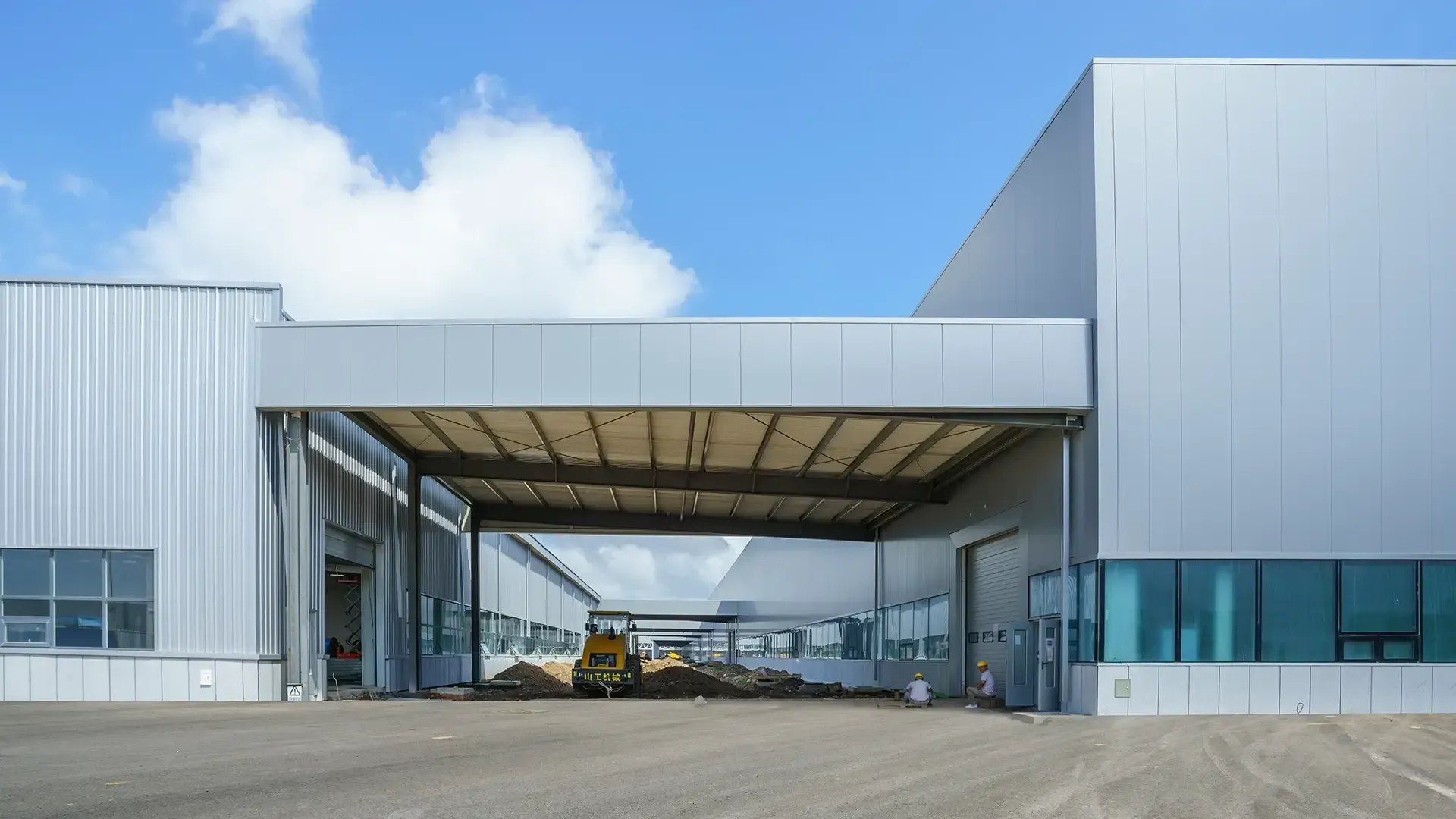 Exterior view of a large, modern industrial building with open entrances under a bright blue sky.
