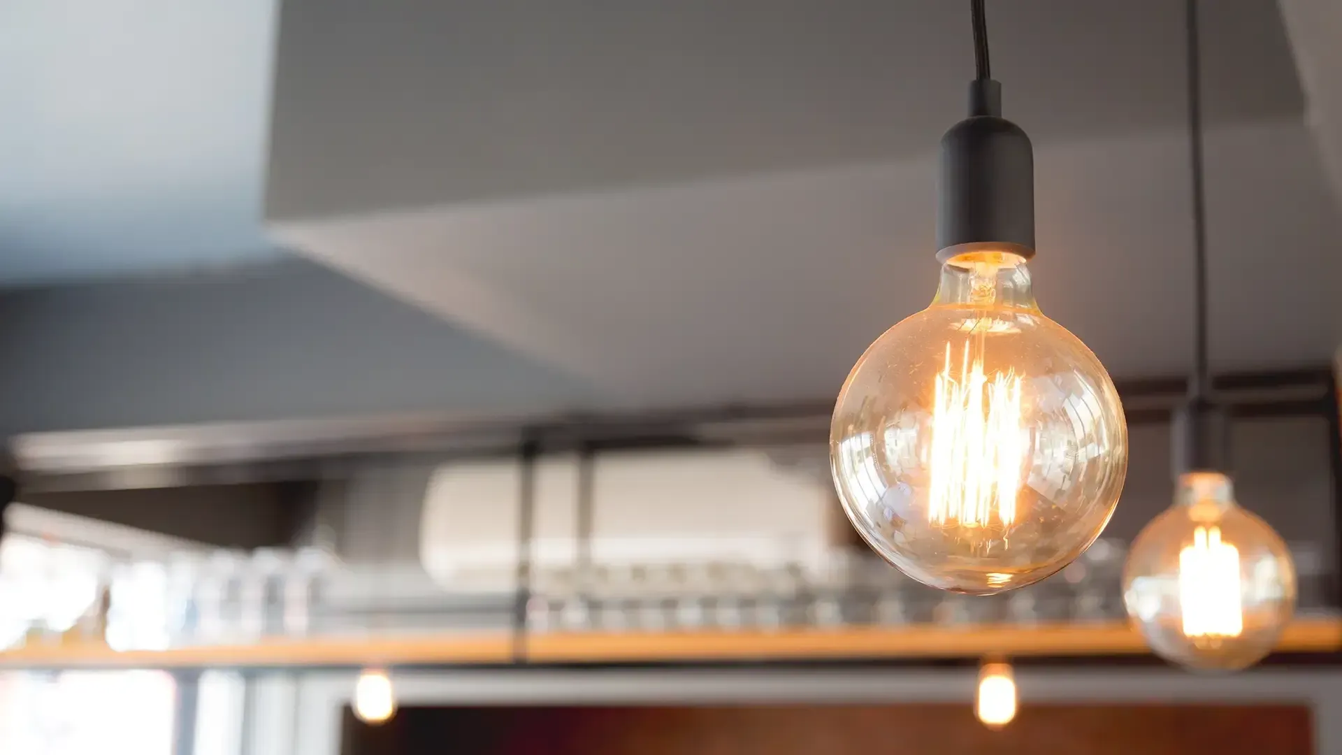 Decorative Edison-style light bulbs hang from a gray ceiling, illuminating a restaurant interior.
