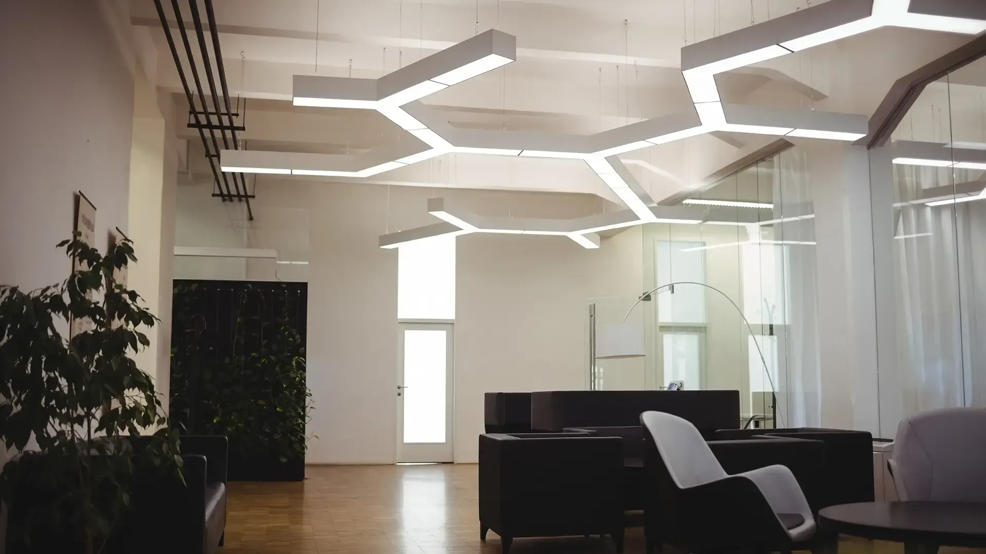 Brightly lit modern office interior with honeycomb-shaped ceiling lights and a lounge area.