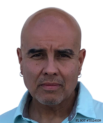Portrait of a bald man with a goatee, wearing hoop earrings and a light blue shirt, looking at the camera.