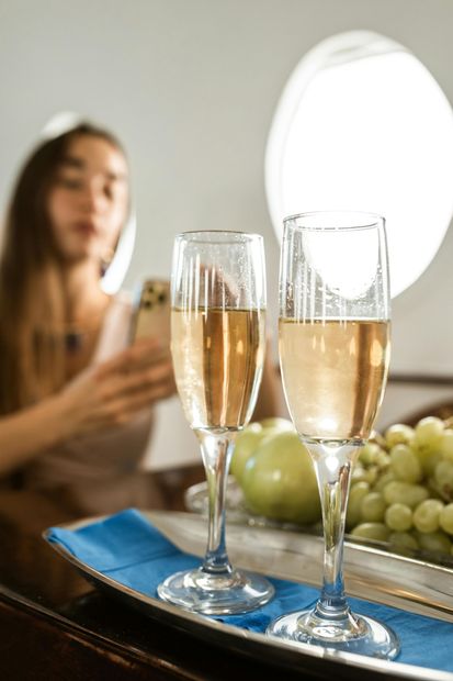 Two champagne flutes on a table with grapes and a blurred woman in the background