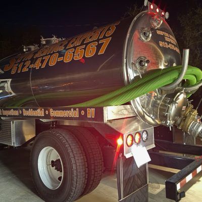 A shiny septic tank truck with business name and phone number in front of a dark setting.