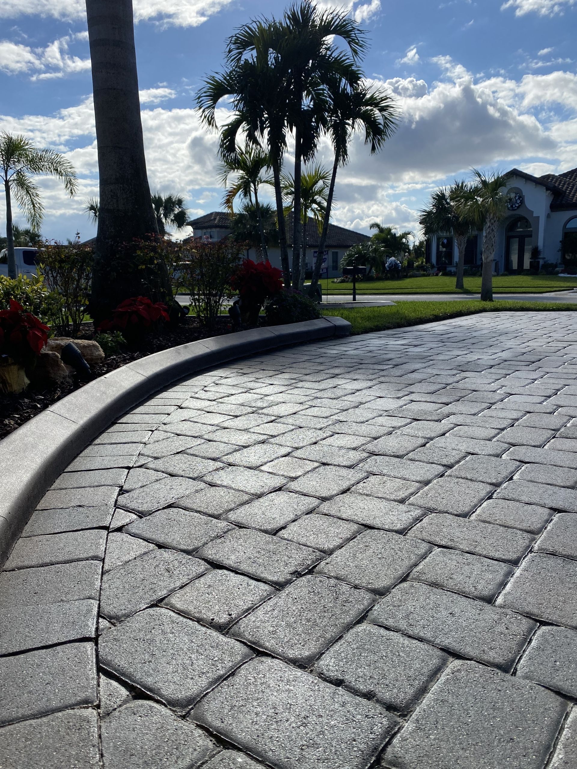 A brick walkway leading to a house with palm trees in the background.
