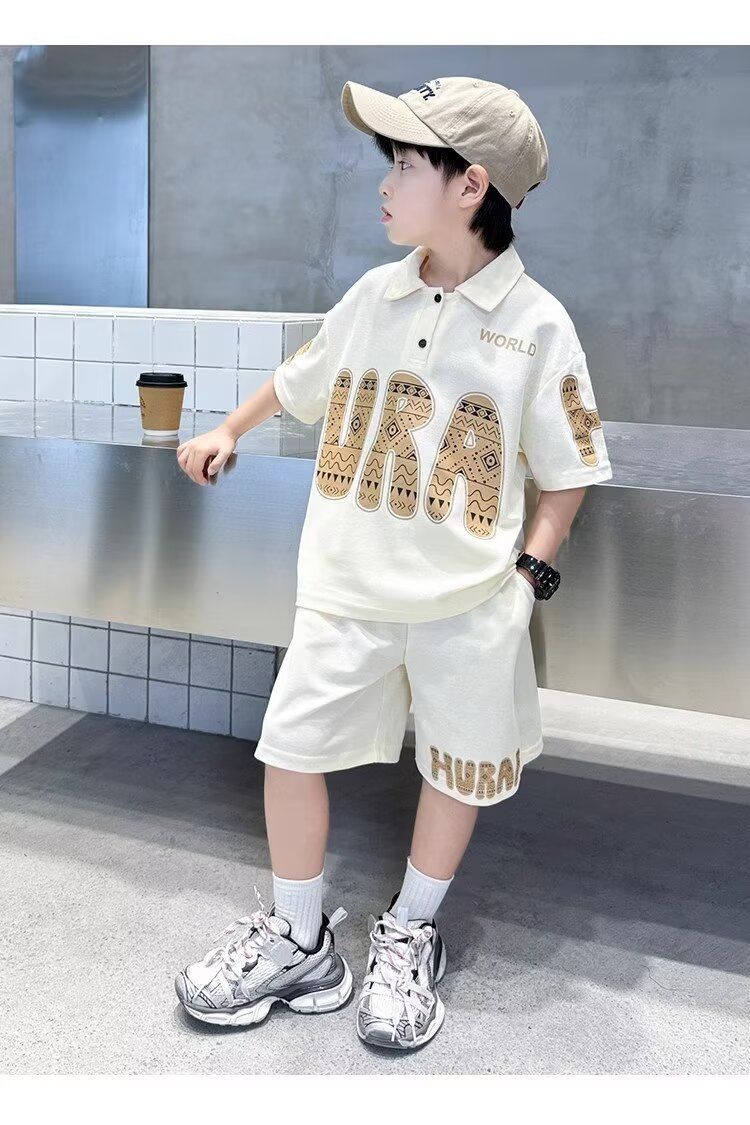 一個穿著白色 Polo 衫和短褲的小男孩站在牆邊。