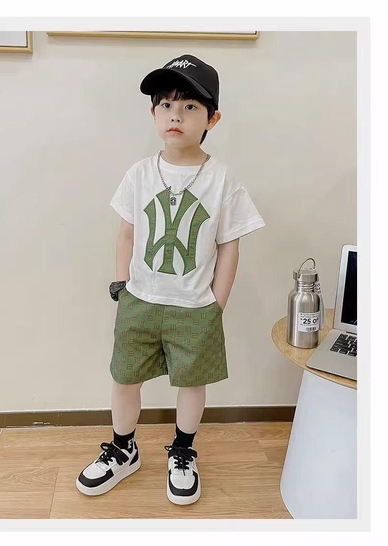 一個穿著白色 T 恤和綠色短褲的小男孩站在桌子旁邊。