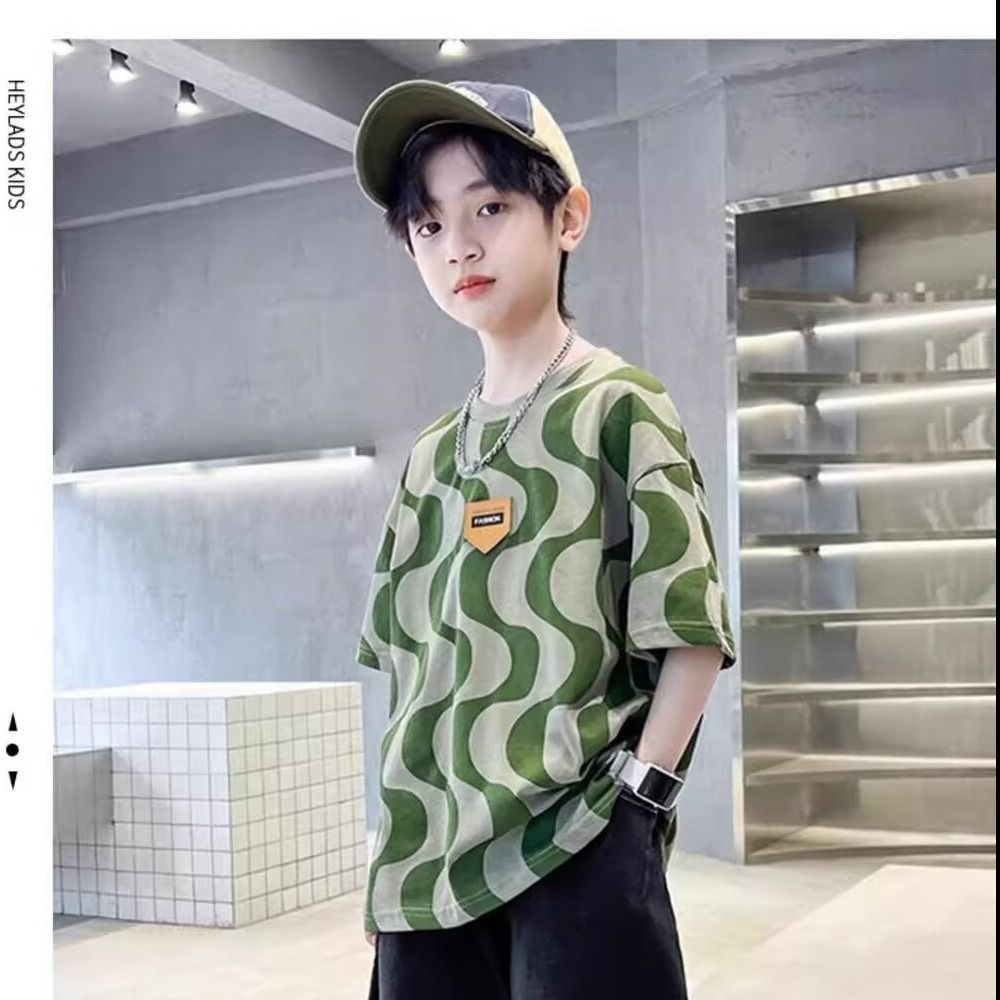 一個穿著綠色 T 恤和戴著帽子的小男孩站在房間裡。