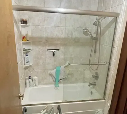 A tiled bathtub shower with glass sliding doors, a mounted hand-held showerhead, and corner shelving holding toiletries.