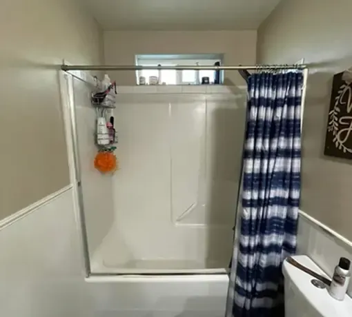 A shower stall with a white surround and a blue-and-white striped curtain, set against a beige wall.