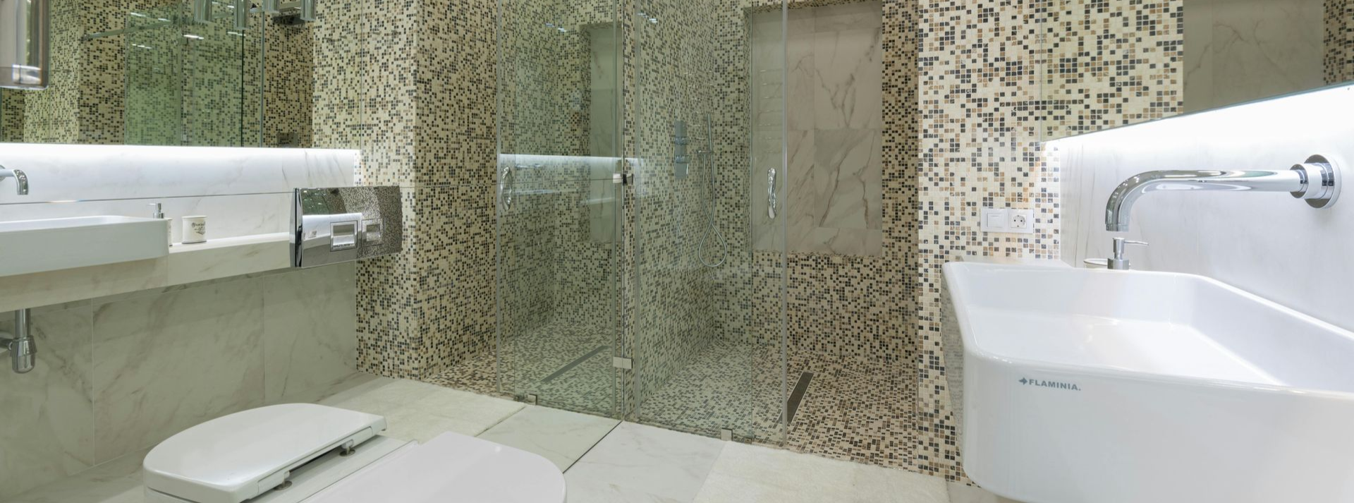 A modern bathroom with two white wall-mounted sinks, a glass-enclosed shower, and decorative pebble-tiled walls.
