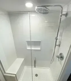 A modern white walk-in shower with a rain showerhead, a glass partition, a built-in bench, and a recessed wall shelf.