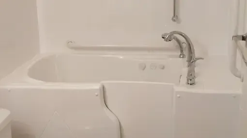 A white walk-in bathtub with a side-entry door, silver faucet, and wall-mounted grab bars in a bathroom.