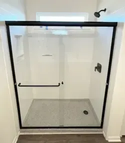 A walk-in shower with white walls, a gray base, clear glass door, and matte black fixtures against a dark floor.