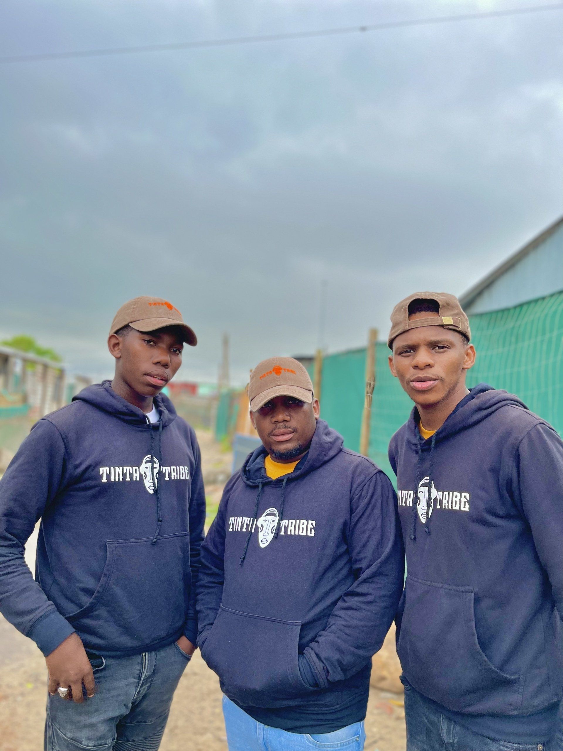 Three men wearing hoodies and hats are standing next to each other