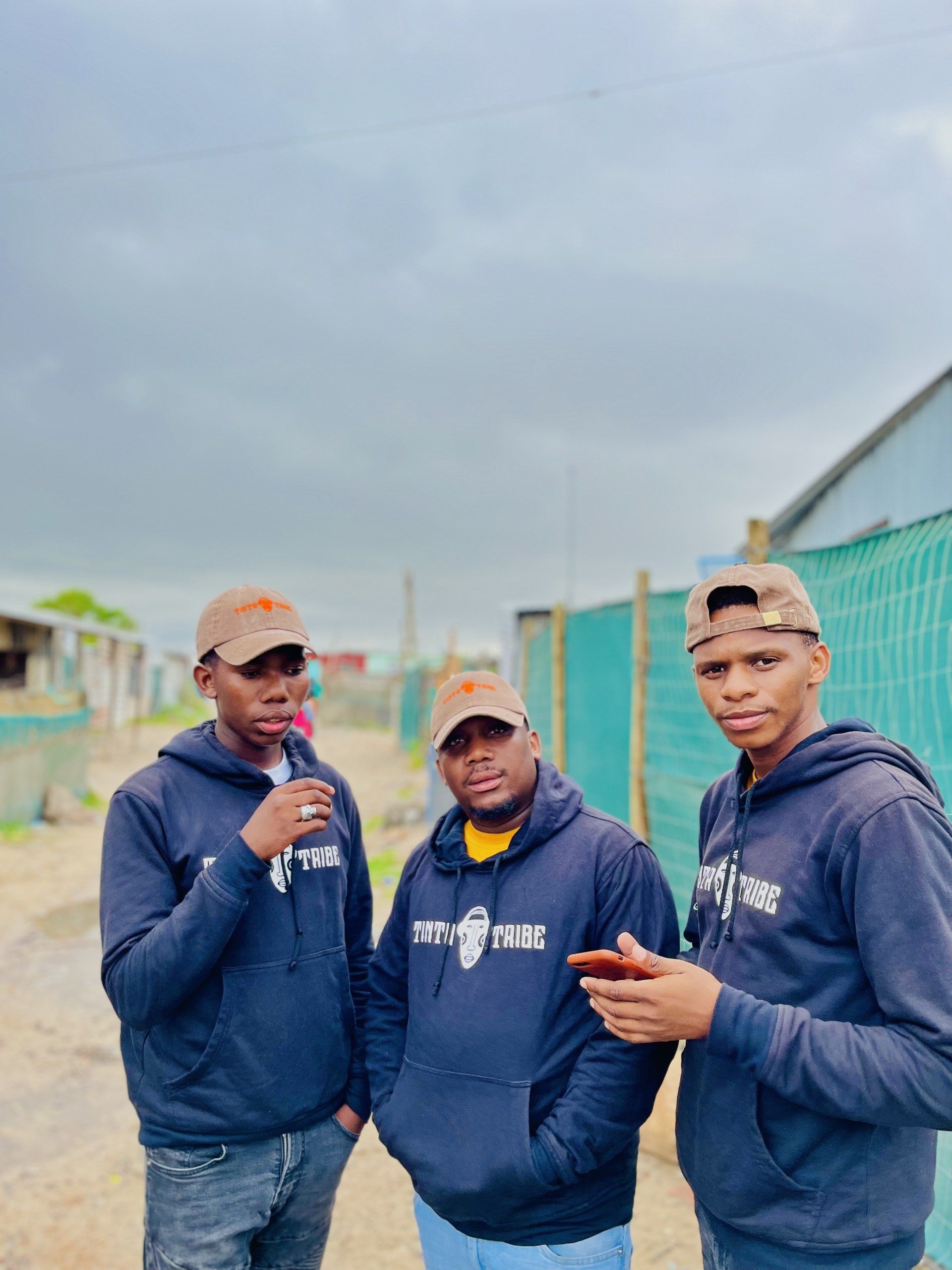 Three men are standing next to each other in front of a fence.
