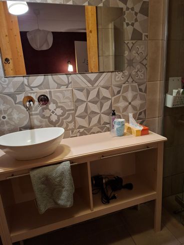 Badkamer met decoratieve tegels, een witte wastafel, een licht houten badmeubel en een spiegel.