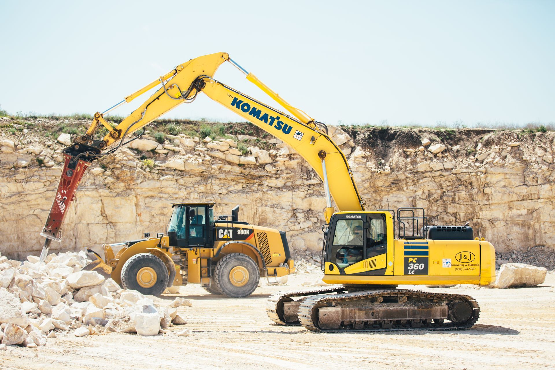A yellow komatsu excavator is moving rocks in a quarry.