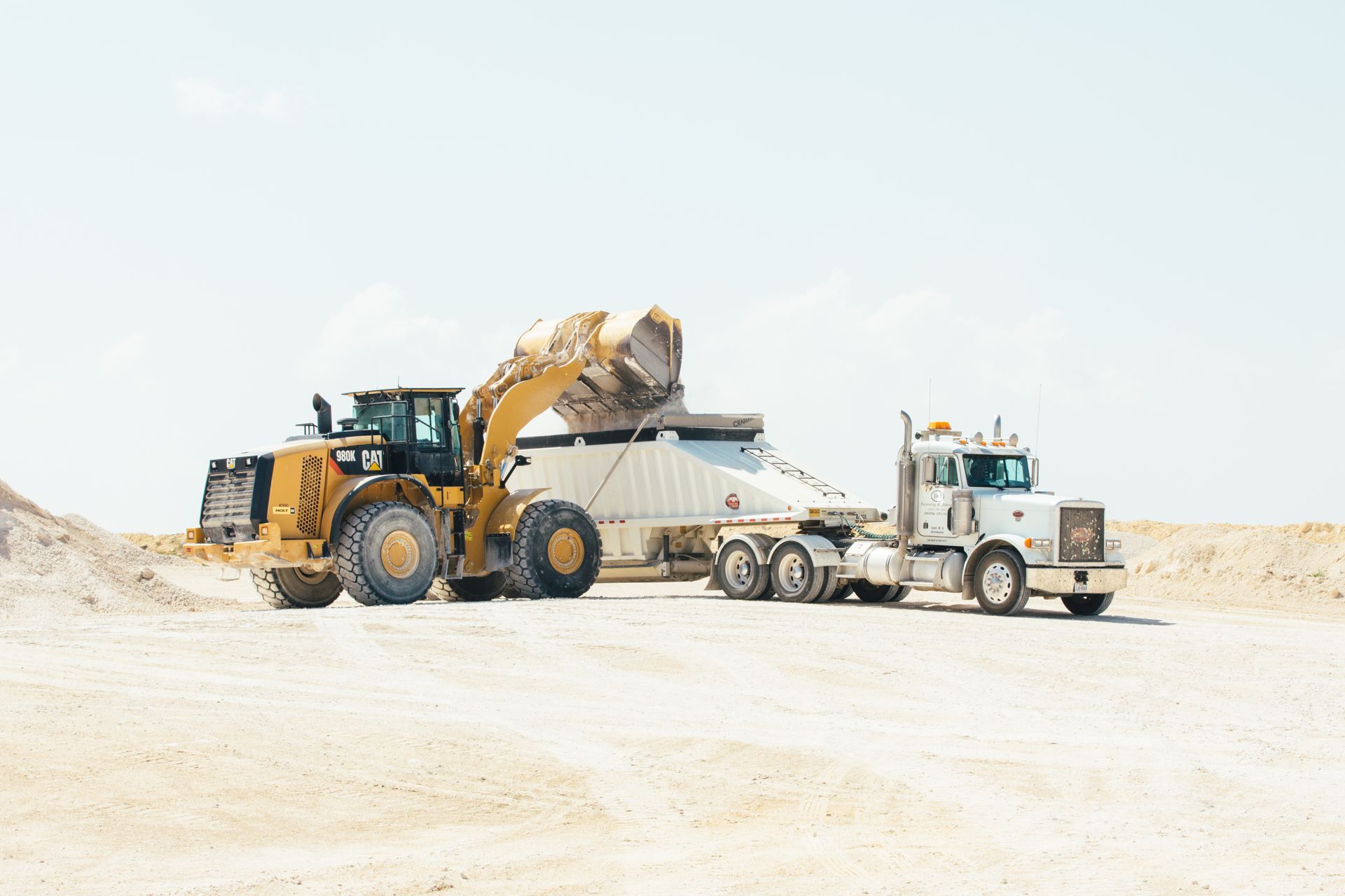 A bulldozer is loading a dump truck with sand.