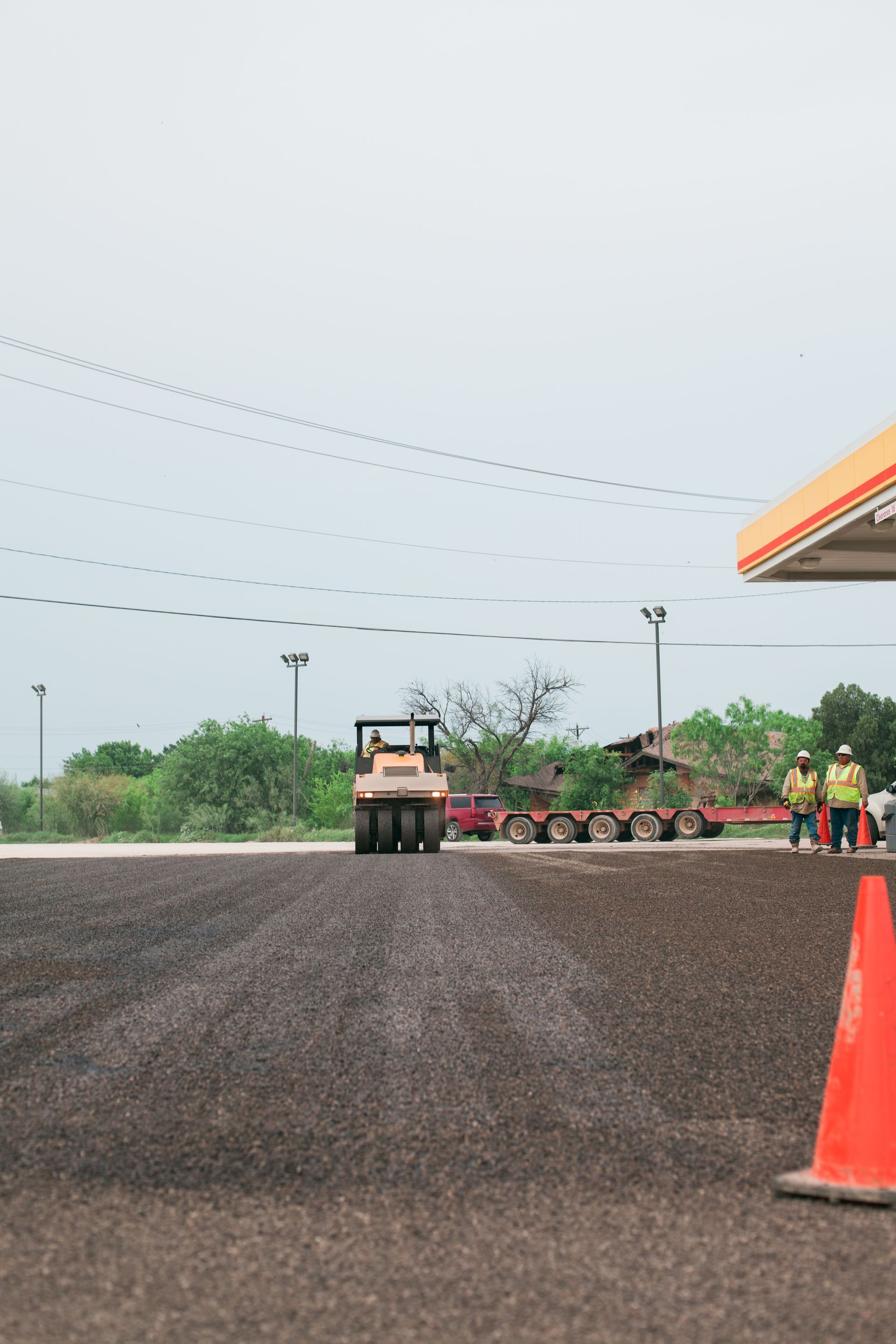 A group of construction workers are working on a road next to a gas station.