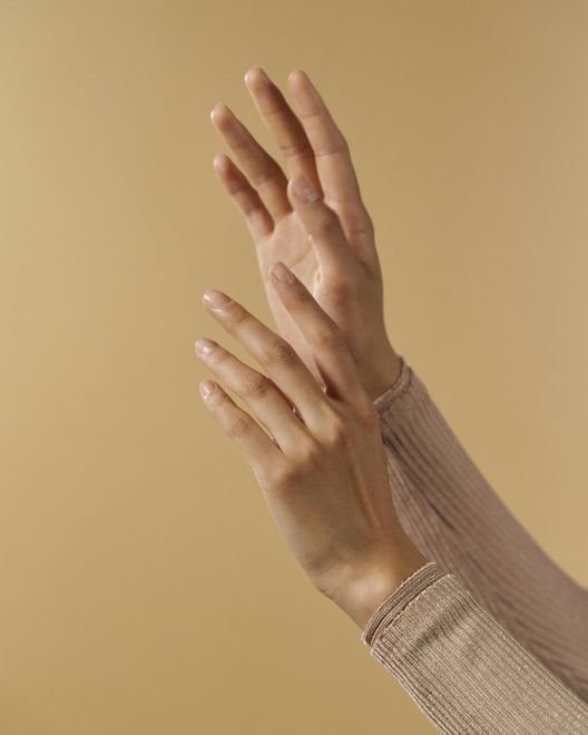 Hands with long, slender fingers, palms up, against a tan backdrop.