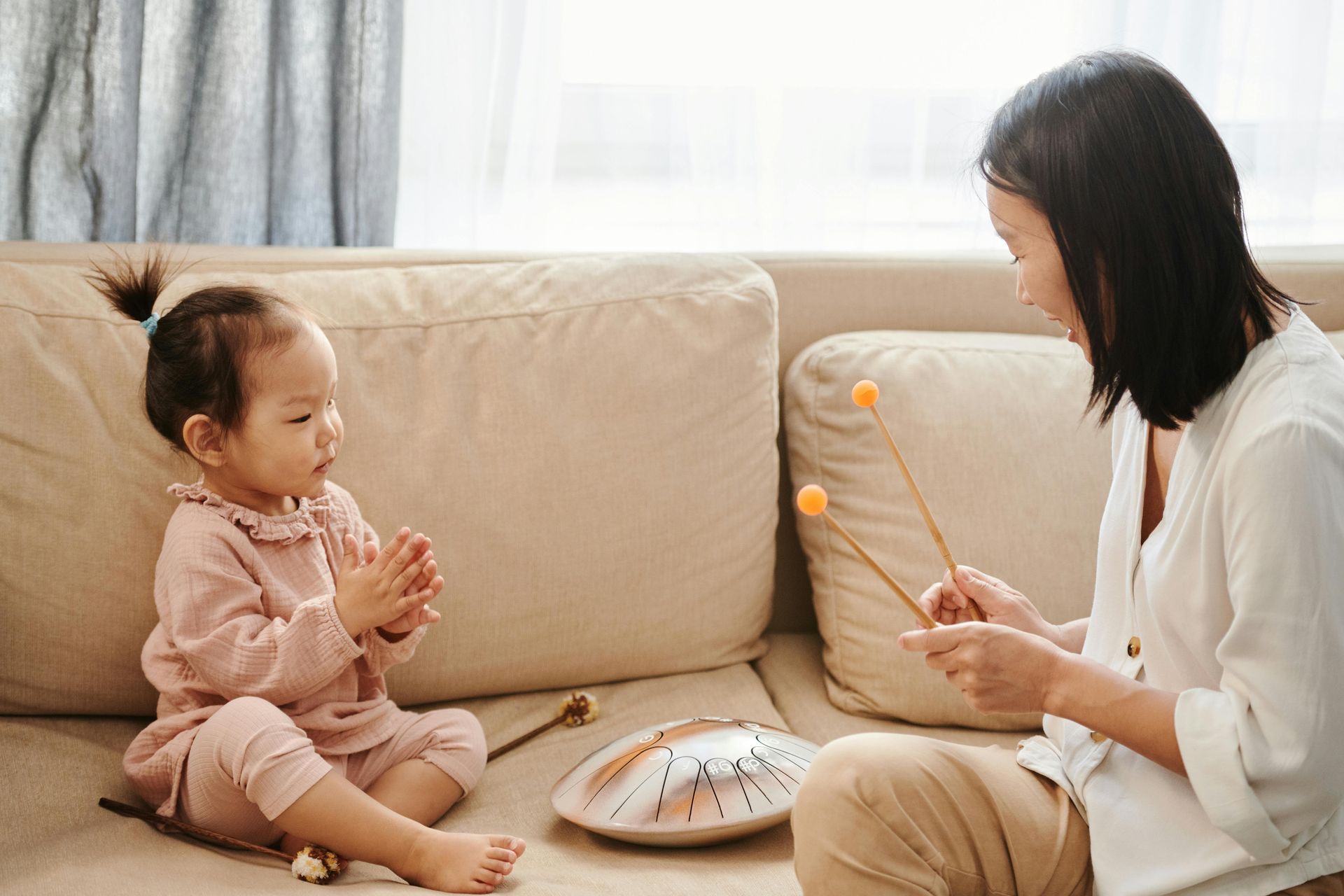Woman playing mallet instrument, toddler clapping on couch.