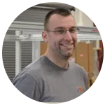 A man wearing glasses and a grey shirt is smiling in a circle.