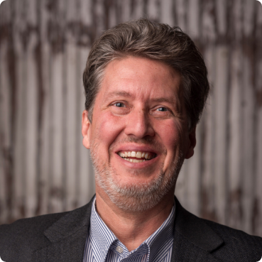 A man in a suit and striped shirt smiles for the camera