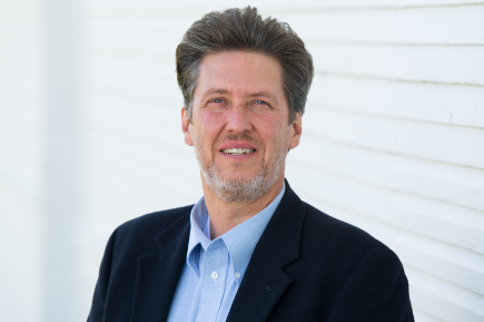 A man in a suit and blue shirt is smiling for the camera.