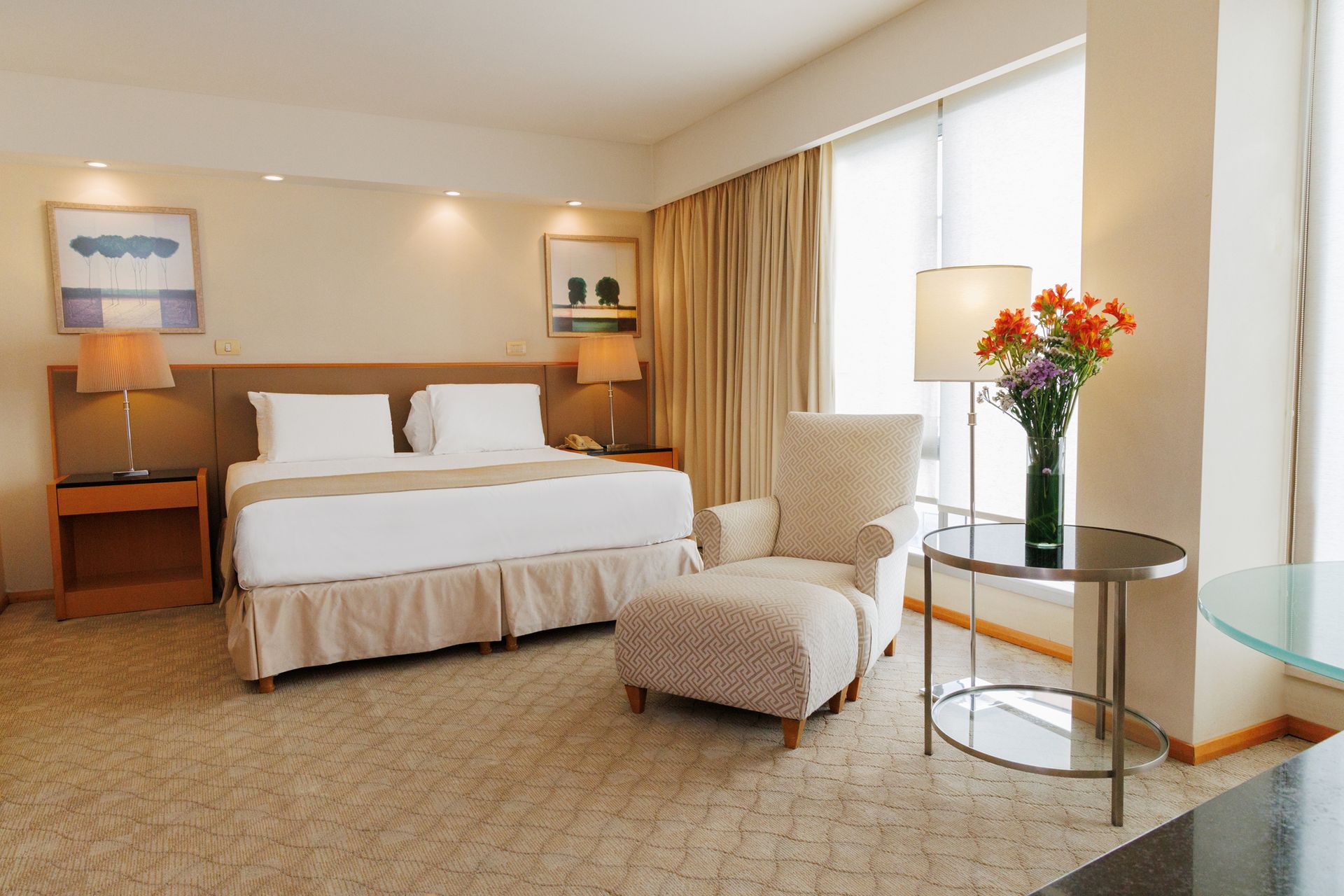 Una habitación de hotel con una cama, una silla, una mesa y un jarrón de flores.