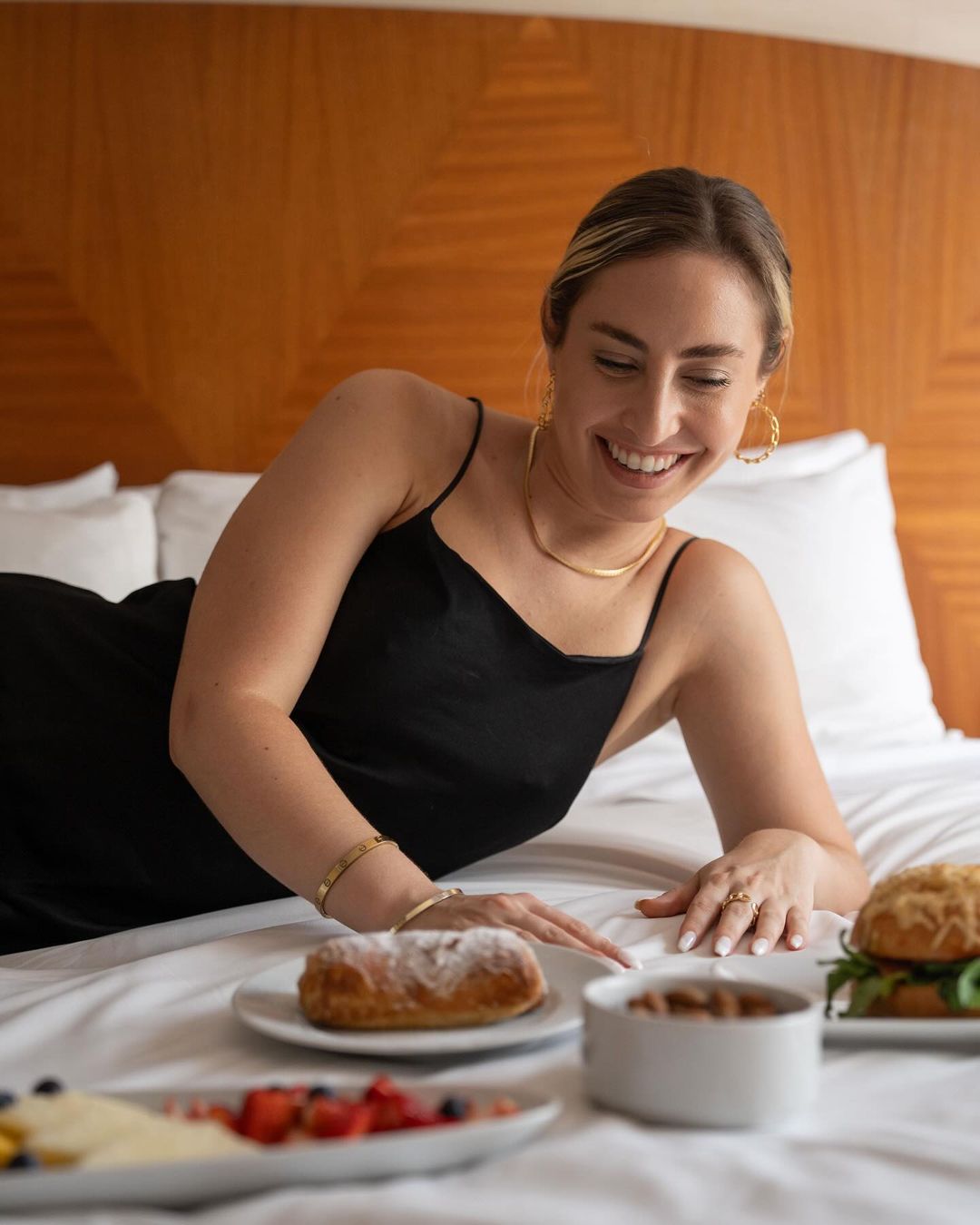 Una mujer está acostada en una cama con platos de comida encima.