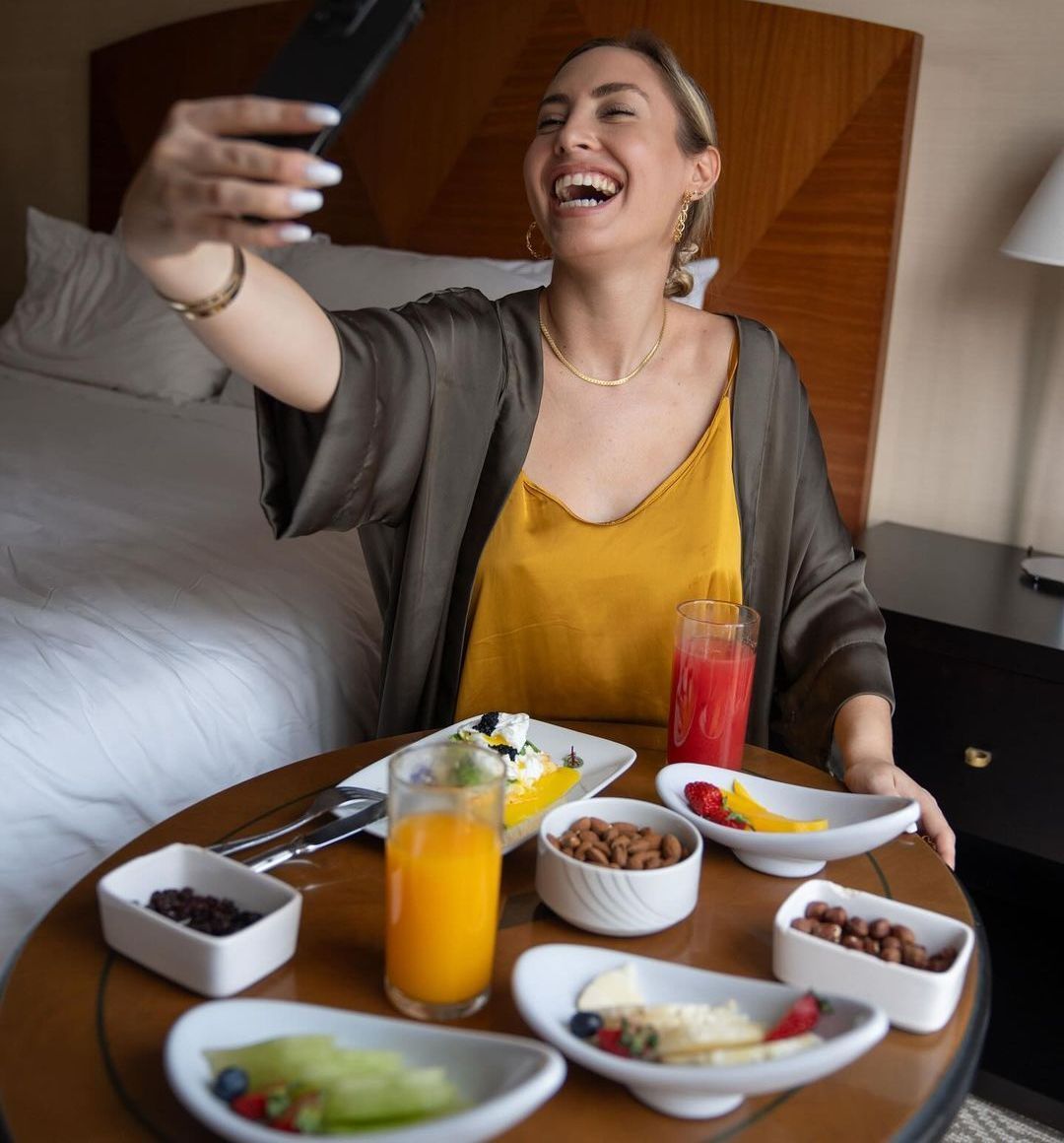 Una mujer se toma una selfie mientras está sentada en una mesa con comida.