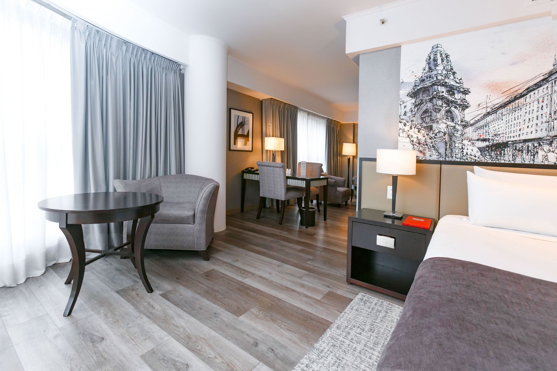 Una habitación de hotel con una cama, mesa, sillas y una gran ventana.