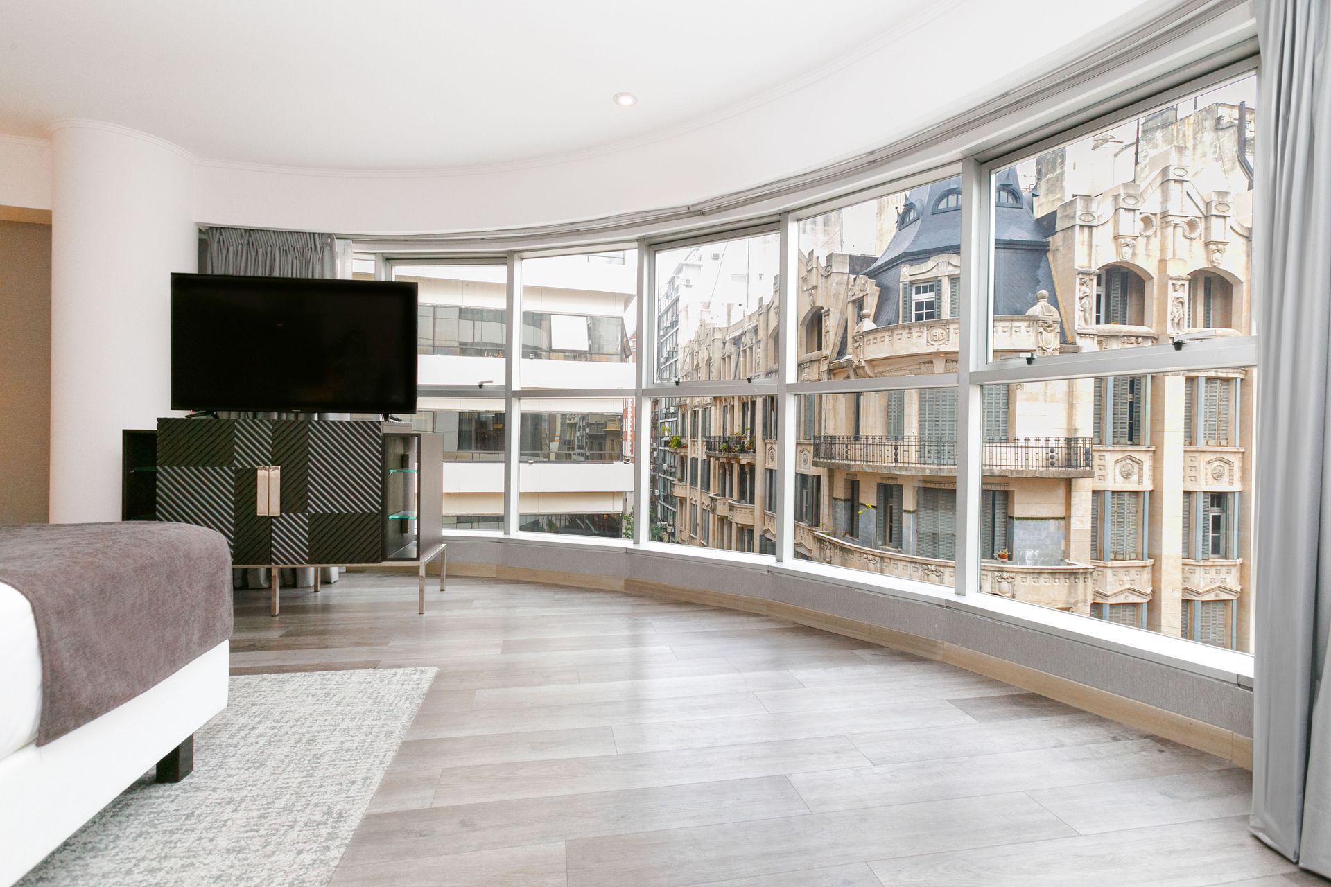 Un dormitorio con cama, televisión y grandes ventanales.