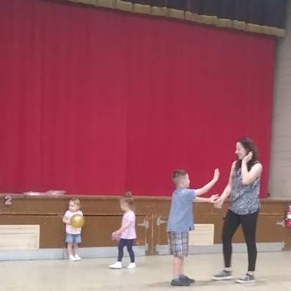A woman and two children are playing with a ball in a gym.