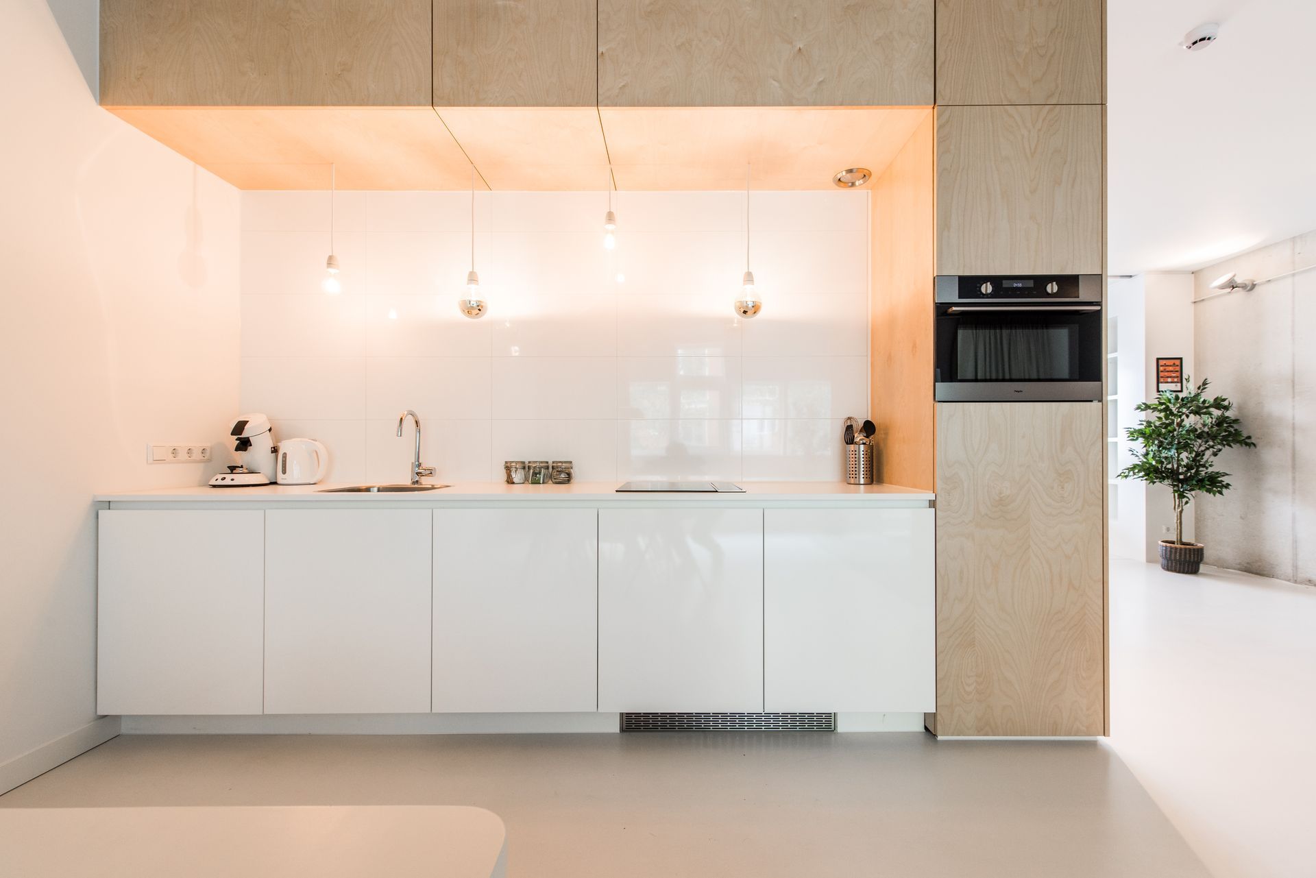 Moderne witte keuken met lichte houten accenten; oven, spoelbak en hanglampen.