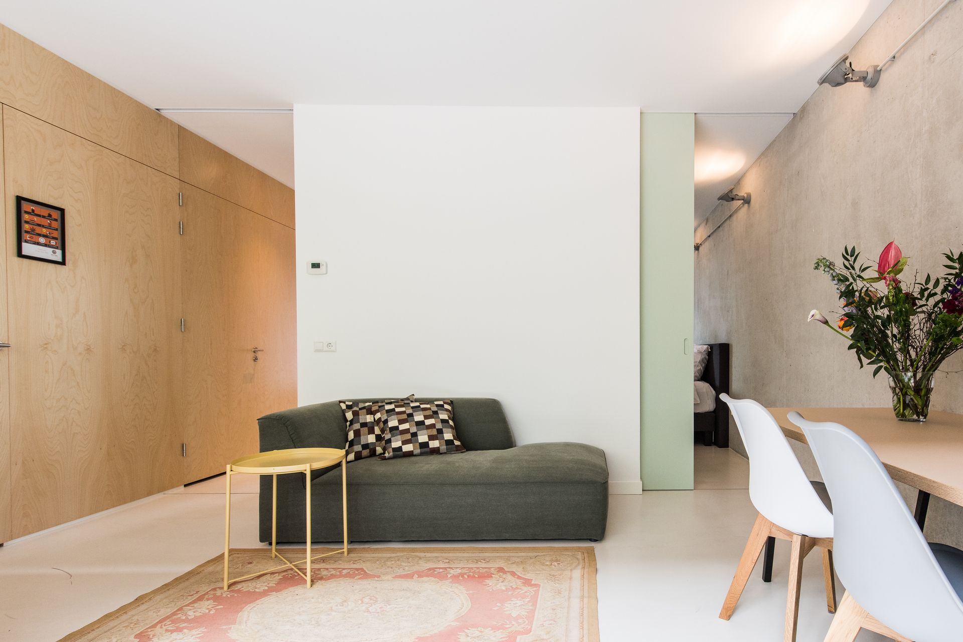 Moderne woonkamer met olijfgroene bank, houten lambrisering en een eettafel.