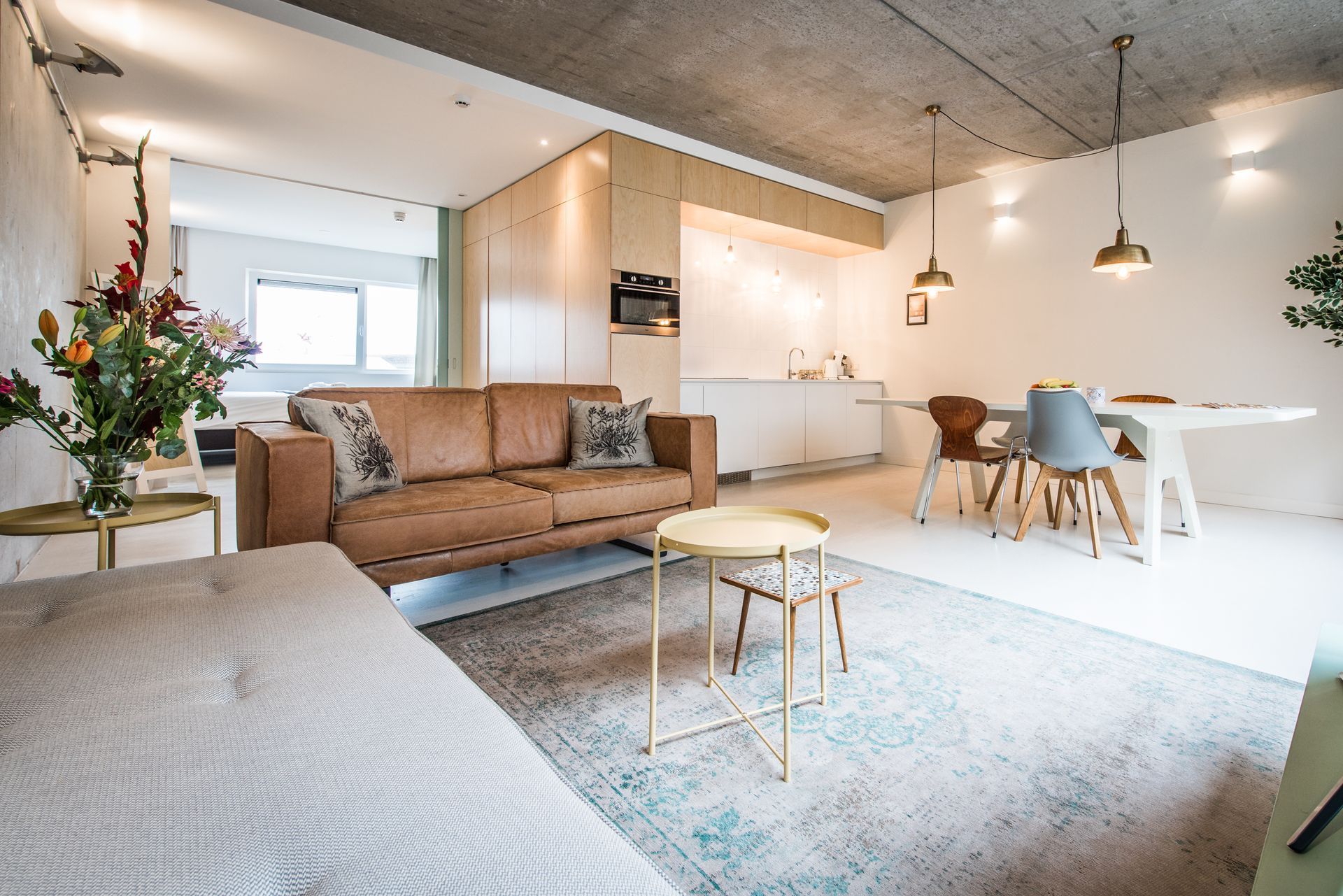 Moderne open woonkamer met beige bank, eethoek en witte muren; gouden accenten en bloemstuk.