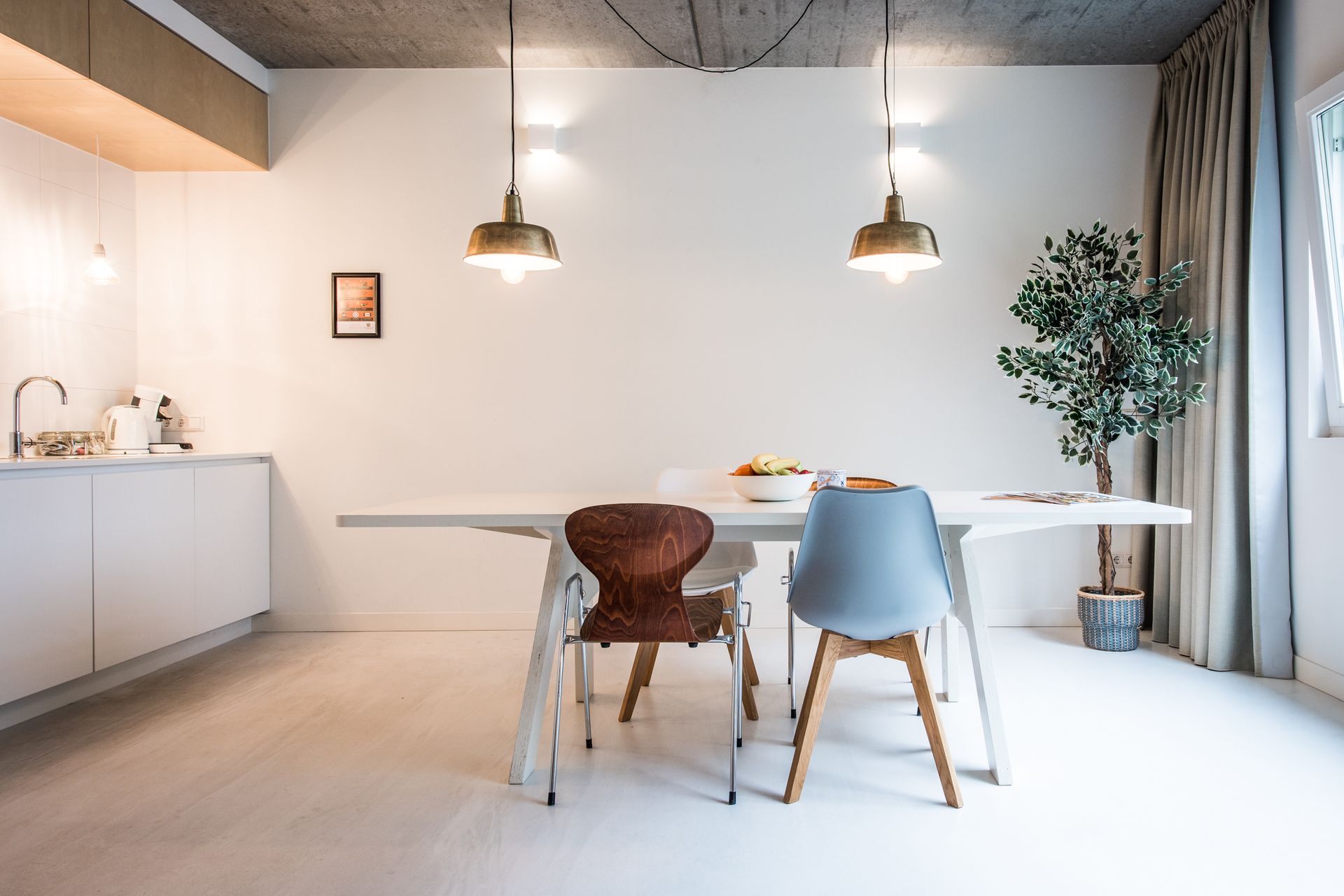 Eetkamer met een witte tafel, twee hanglampen en diverse stoelen.