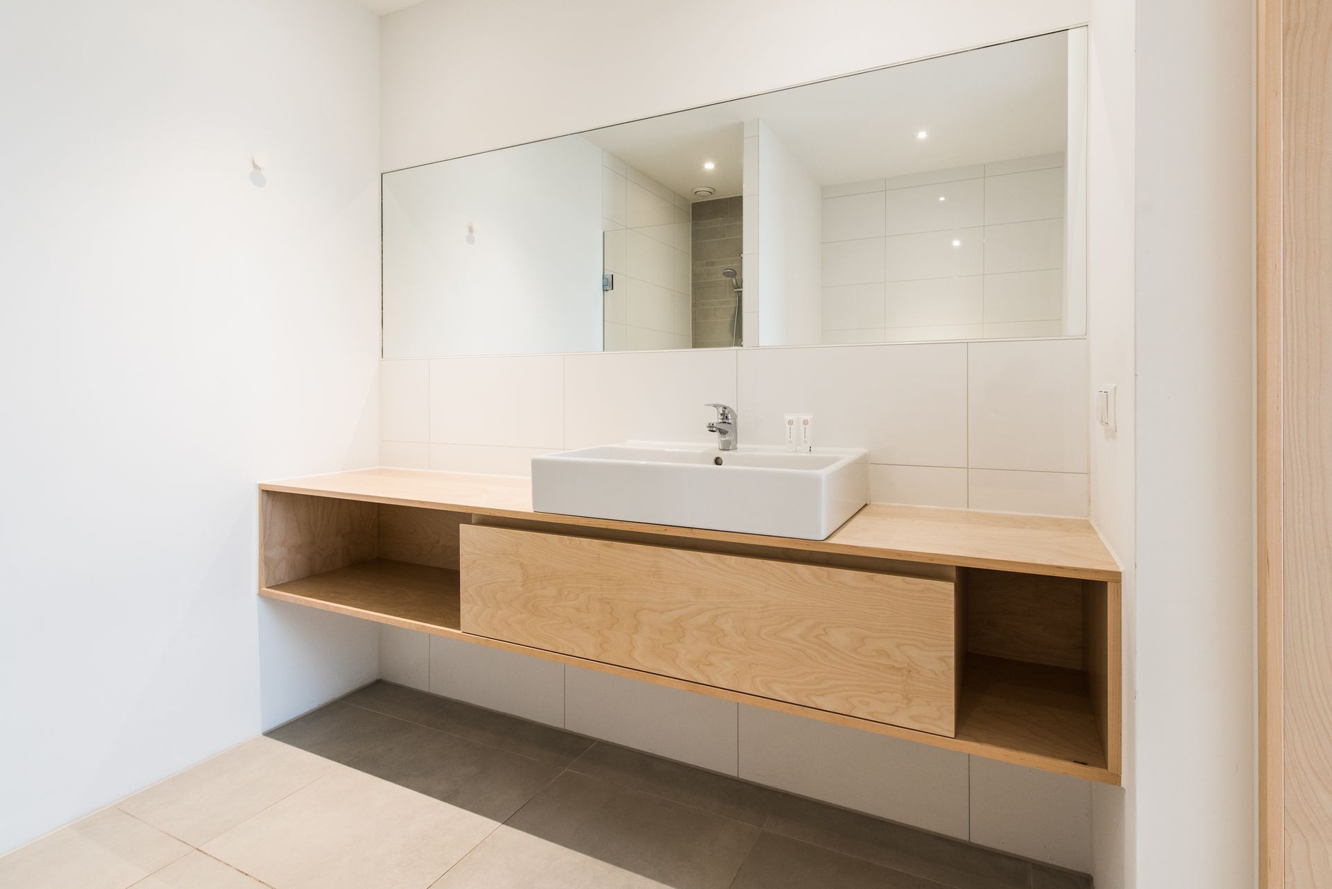 Moderne badkamer met een licht houten badmeubel, witte wastafel en grote spiegel.