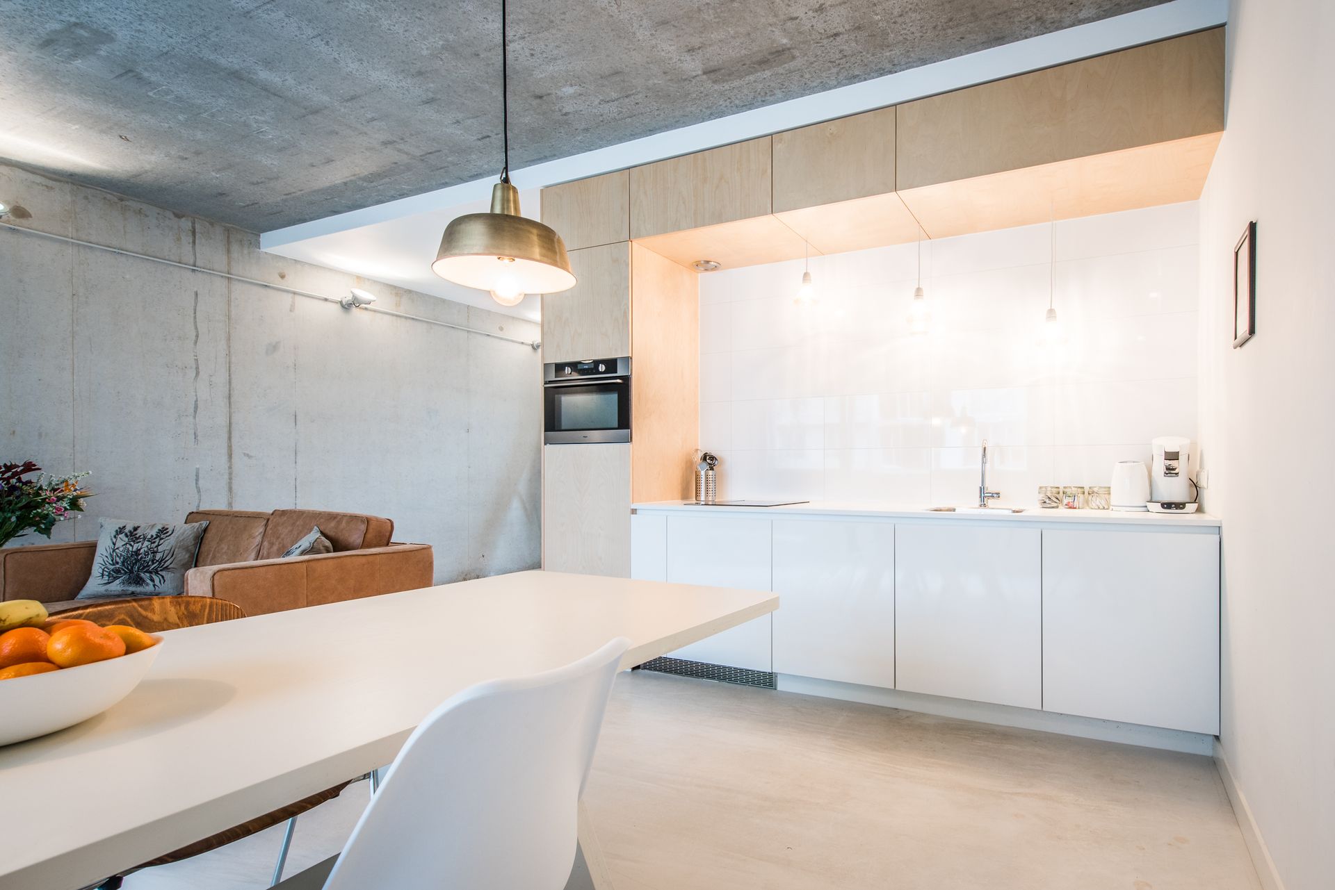 Moderne, minimalistische keuken met witte kasten, betonnen muren en een eettafel.