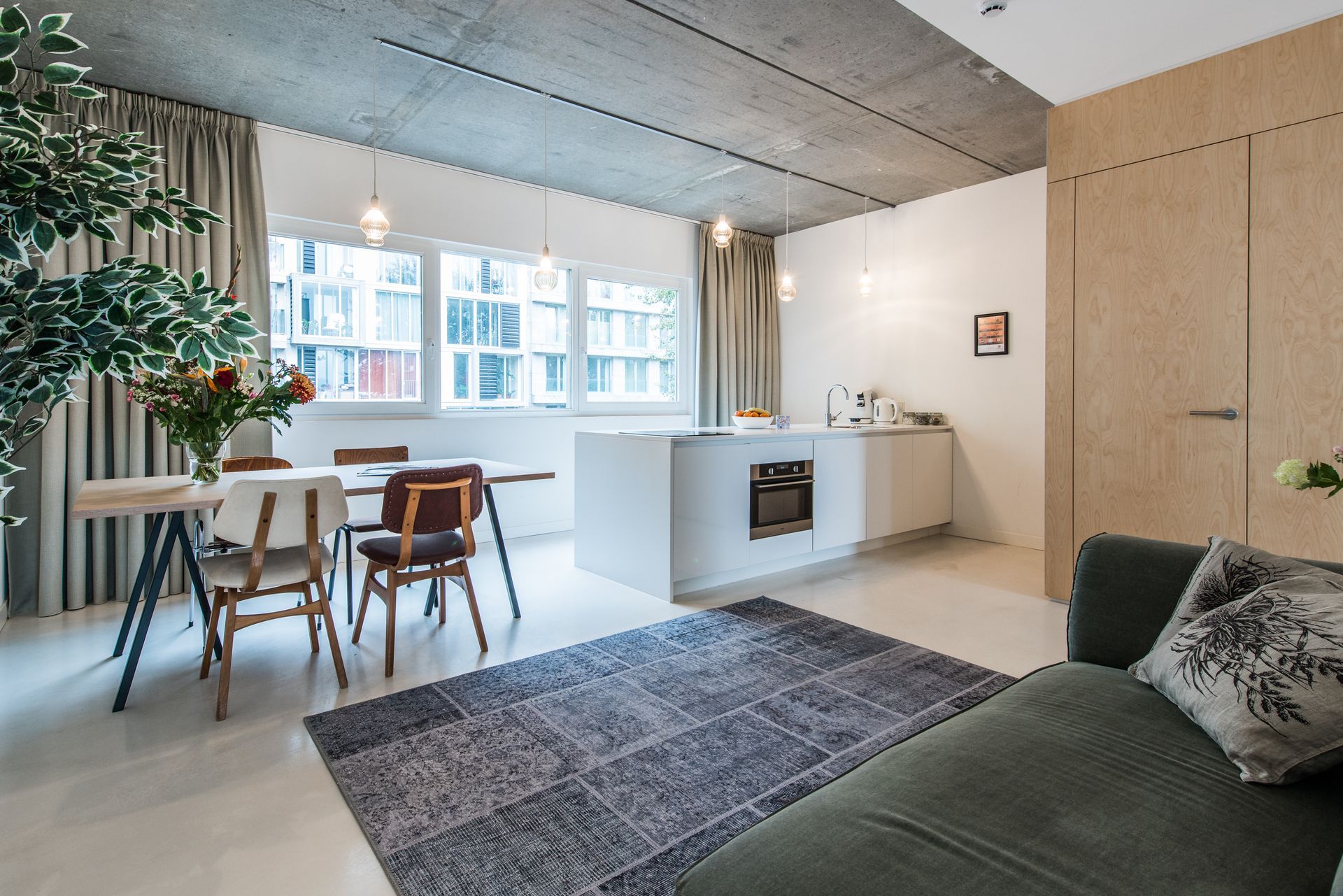 Modern appartement met open indeling, eettafel, kookeiland, bank en grijs vloerkleed.
