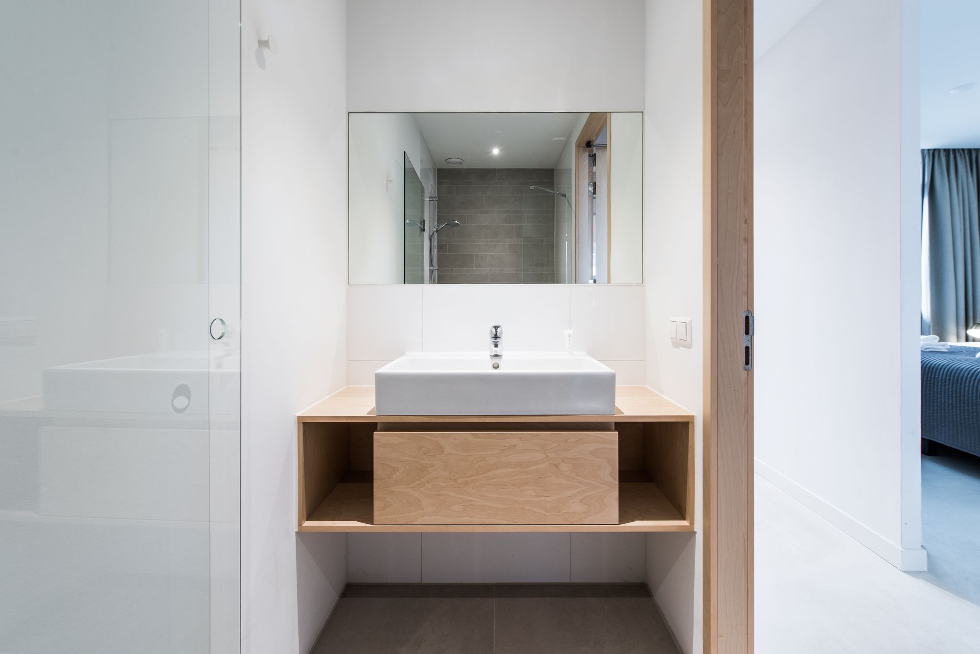 Moderne badkamer met een rechthoekige wastafel, houten kast en grote spiegel.