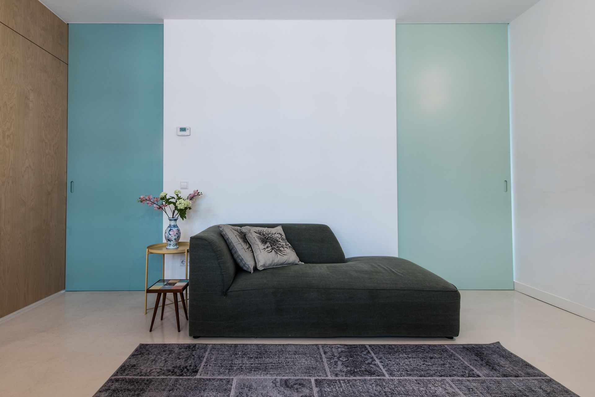 Donkergroene bank in een moderne kamer met blauw-witte muren, een vloerkleed en een tafeltje met bloemen.