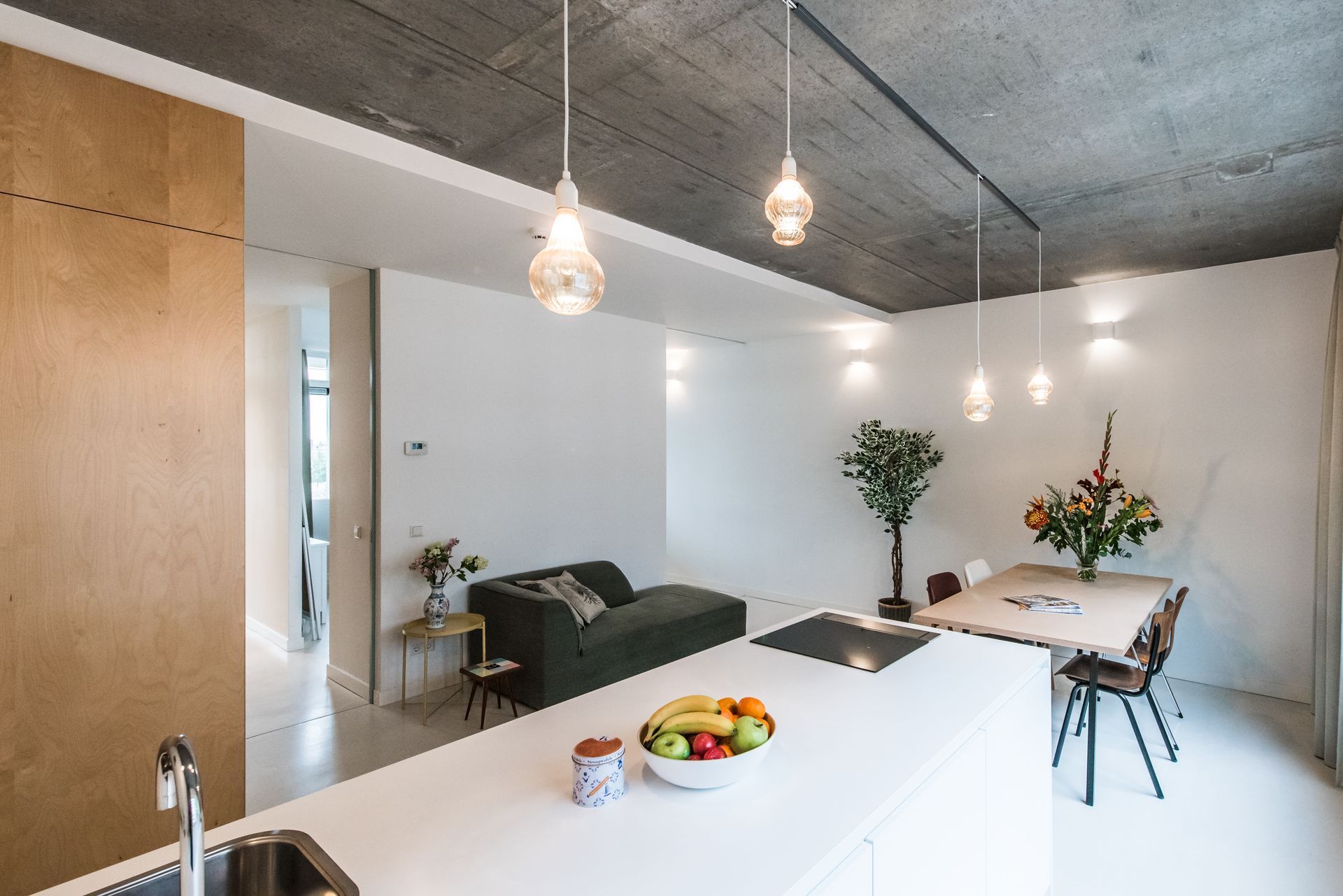 Modern interieur met kookeiland, zithoek, eettafel en betonnen plafond.