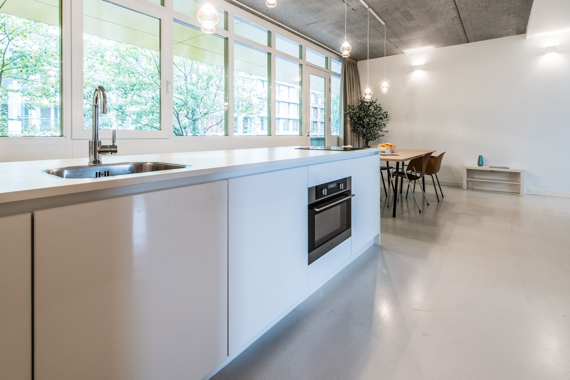 Moderne keuken met wit kookeiland en roestvrijstalen spoelbak, grote ramen en een oven.