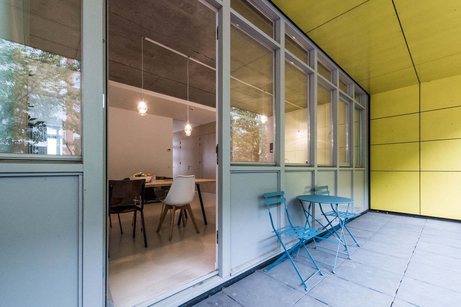 Buitenterras met lichtblauwe meubels en gele muren, met uitzicht op een eetgedeelte.