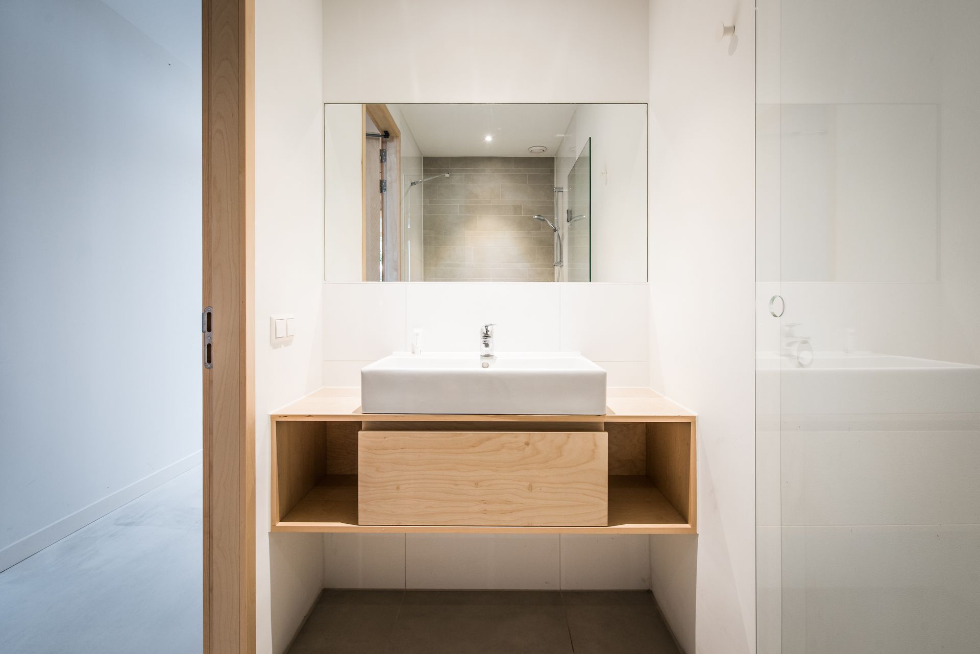 Moderne badkamer met witte muren, houten badmeubel, vierkante wastafel en grote spiegel.