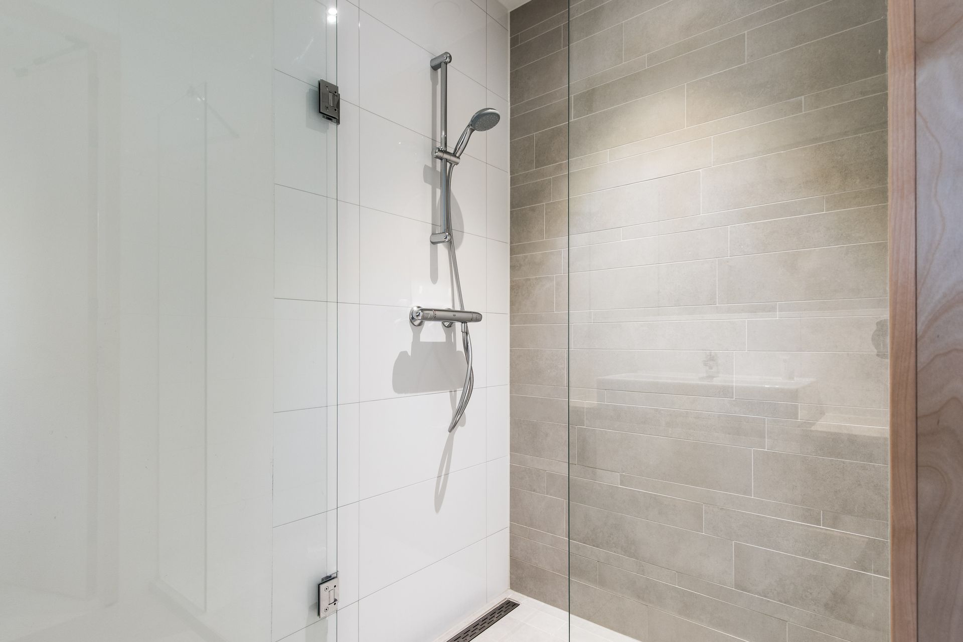 Douchecabine met glazen deur, chromen douchekop en wit-grijze tegelwanden.